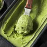 Loaf pan with homemade creamy matcha lychee ice cream being scooped out.