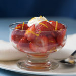 Glass bowl of strawberries topped with a dollop of sweetened whipped cream and garnished with orange zest