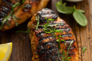 Wooden cutting board with perfectly moist reverse sear chicken breasts garnished with lemon and fresh herbs