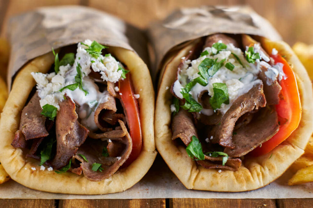 Closeup of two Better Than Takeout Gyros And Tzakiki Sauce wrapped in brown paper.