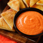 Bowl of spicy roasted red pepper and feta dip with pita triangles