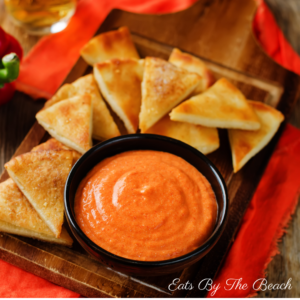 Spicy roasted red pepper and feta dip in bowl with pita triangles on the side