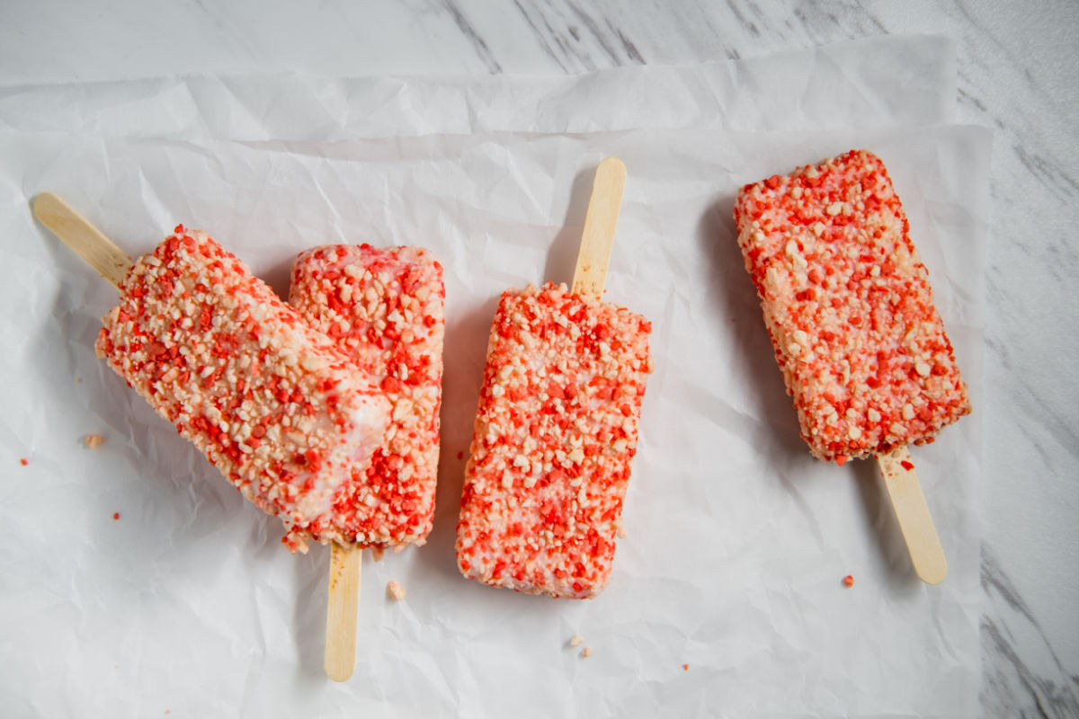 Strawberry shortcake ice cream bars with cake crumbles on a white marble slab.