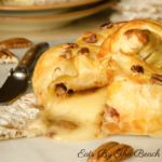 Wheel of brie topped with pecans, brown sugar and cinnamon, wrapped in puff pastry and glazed with honey and additional chopped pecans. An elegant appetizer recipe.