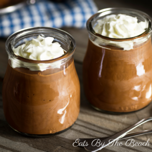 Small jars of the classic dessert recipe for Mousse au Chocolat garnished with a dollop of fresh whipped cream.