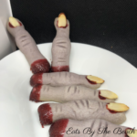 A plate of gray shortbread cookies in the shape of monster fingers, with red jam on the end to look like they are severed. A holiday cookie that is both creepy and delicious.