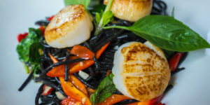 A plate of stir-fried black squid ink pasta, red peppers, carrots and scallops.