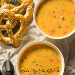 White bowls of the best cheese soup full of minced vegetables and served with soft pretzels.