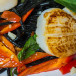 A plate of stir-fried black squid ink pasta, red peppers, carrots and scallops.