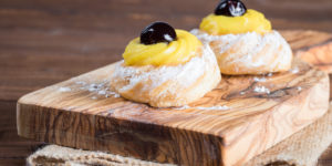 A classic Italian pastry, this wooden board with two zeppole pastries filled with almond scented Italian pastry cream and garnished with a syrupy amarena cherry.