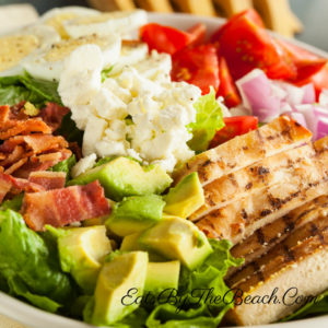 A cobb salad with grilled chicken, egg, bacon, avocado, tomato, onion, and feta cheese with a homemade Catalina-Style French dressing.
