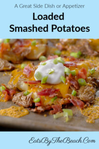 A plate with a baby potato that has been boiled, smashed into a patty and then browned in garlic butter. It's then baked with cheddar cheese and bacon, then garnished with sour cream and chopped green onion. This loaded smashed potato has all the flavors of your favorite loaded baked potato.