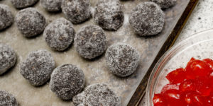 Tray of decadent chocolate bourbon balls coated with superfine sugar and garnished with a maraschino cherry half. A boozy no-bake treat perfect for a Kentucky Derby party or holiday cookie tray.