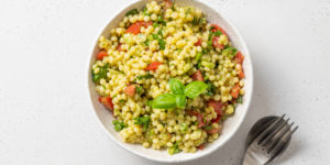 Bowl of toasted Israeli couscous salad with minced fresh vegetables, herbs, and zesty lemon/basil vinaigrette.