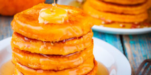 A stack of pumpkin spice hoecakes with hot honey maple butter and maple syrup luxuriously dripping down the sides.