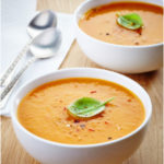 A hot, steaming bowl of creamy Easy Butternut Squash Soup garnished with cracked red and black pepper and a fresh basil leaf.