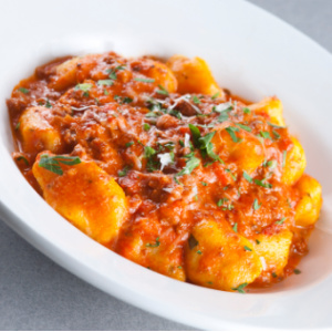 Bowl of homemade Ricotta Gnocchi In Easy Pomodoro Sauce and garnished with a sprinkle of fresh herbs.
