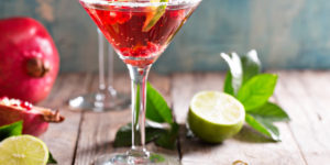 A crimson colored Pomegranate Martini - made with Mandarin vodka, orange liqueur, pomegranate juice, and orange blossom water. It's garnished with a lime slice and pomegranate seeds.