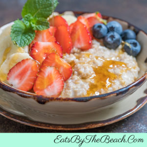 Bowl of warm and heart fruit and honey Irish oatmeal with sliced bananas, sliced strawberries, blueberries, and a drizzle of honey.