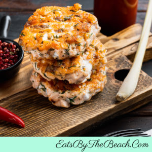 Asian street food at home. This is a stack of Thai Fish Cakes on a wooden board with a bottle of sweet chile sauce on the side.