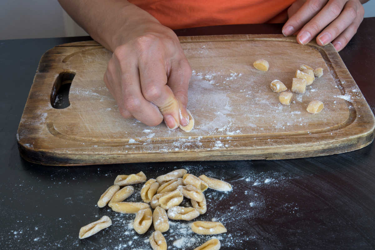 A woman making homemade cavatelli pasta on a wooden board by hand.