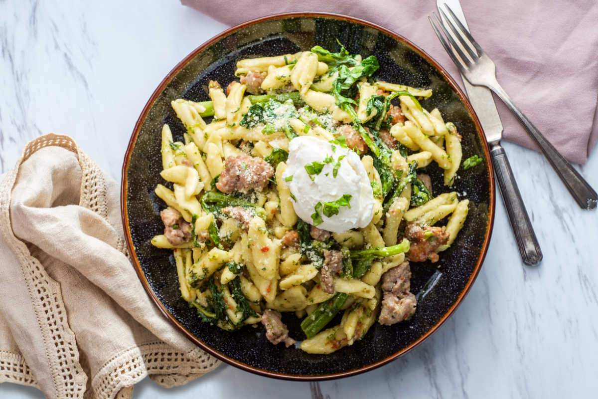 Brown bowl of Cavatelli With Sausage And Broccoli Rabe, garnished with a dollop of fresh ricotta cheese.