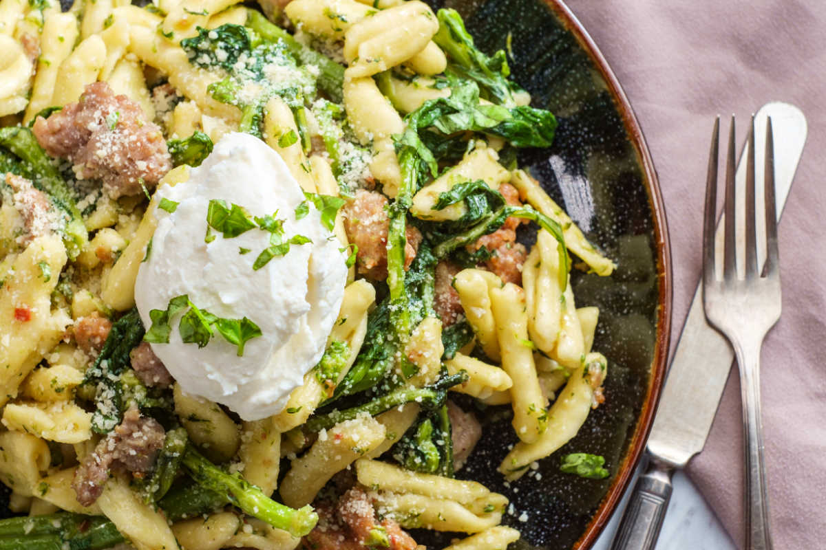 Closeup of a brown bowl of Cavatelli With Sweet Sausage And Broccoli Rabe.