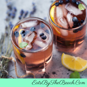 Highball glasses with Lemon Blueberry Lavender cocktails garnished with lemon twists, blueberries, and a sprig of fresh lavender.