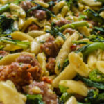 Bowl of tender cavatelli with sausage and broccoli rabe, garnished with a dollop of ricotta cheese and a sprinkle of parmesan.