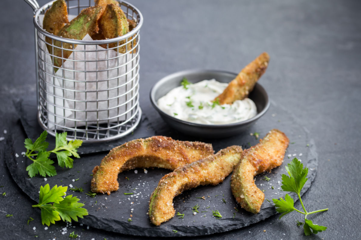 Slate plate of crispy avocado fingers served with a spicy lime crema - slices of avocado are breaded and pan fried and served with a sour cream, cayenne, and lime.