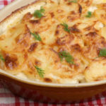 Casserole dish of creamy scalloped potatoes with a golden brown topping and garnished with fresh dill.