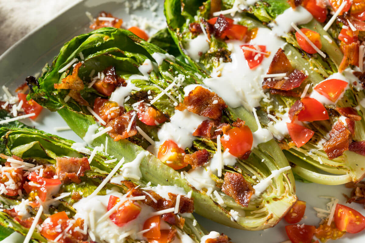 A platter of Grilled Romaine Salad with grilled romaine lettuce, crispy bacon, fresh tomatoes, Parmesan cheese, and a homemade, creamy dressing.