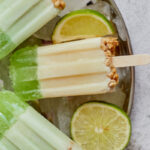 a plate of homemade key lime pie popsicles over ice and garnished with slices of lime