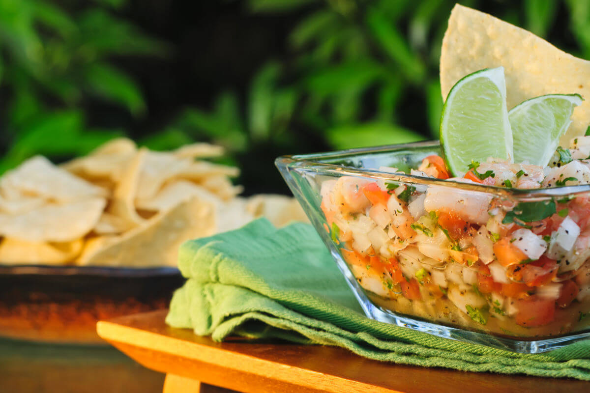 Glass bowl of colorful Mexican Shrimp Ceviche garnished with lime wedges and tortilla chips.