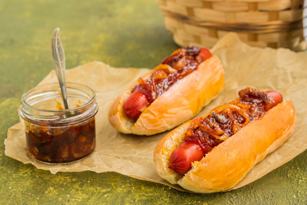 2 NYC-style Dirty Water Dogs with onion sauce on brown paper with a jar of onion sauce on the side