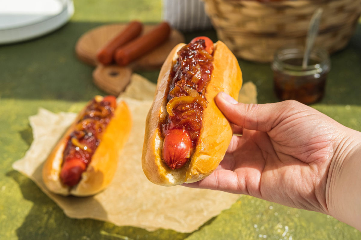 Hand holing a NYC-style dirty water dog with onion sauce