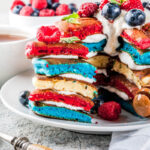 A plate of Patriotic Pancakes - red, white, and blue pancakes topped with French Chantilly Cream, blueberries, raspberries, and a sprig of fresh mint.