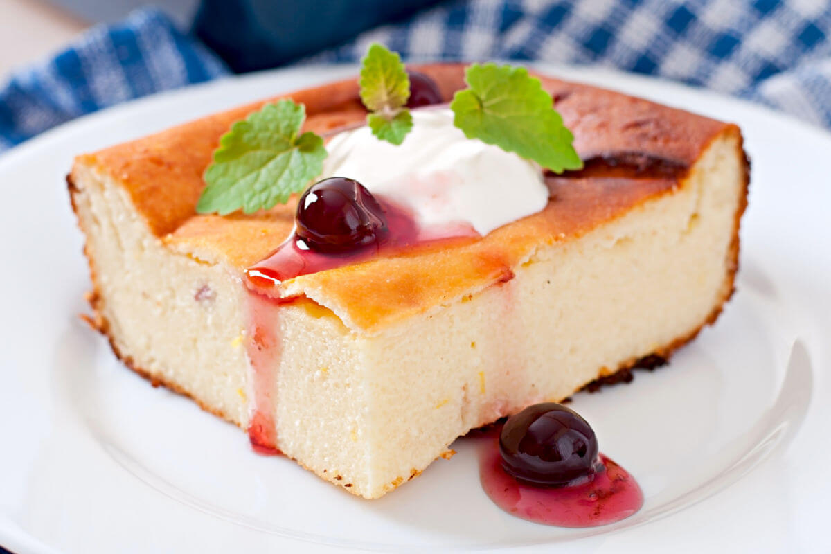 A square of Russian Breakfast Cheesecake garnished with sour cream, blueberries in syrup, and mint sprigs.