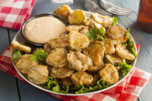 Plate of ridiculously good fried pickles with a side of sauce for dipping.