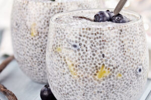 Short glass full of vanilla blueberry chia seed breakfast pudding, garnished with fresh blueberries.