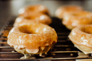 Wire rack of homemade baked maple glazed donuts with the glaze dripping off below the donuts onto the counter.