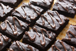 Close up of a platter of dark chocolate avocado brownies, cut into squares and garnished with milk chocolate frosting drizzle.