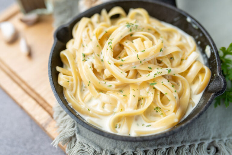 Cast iron skillet with Quick And Easy Fettuccine Alfredo garnished with Parmesan Reggiano cheese and chopped parsley.