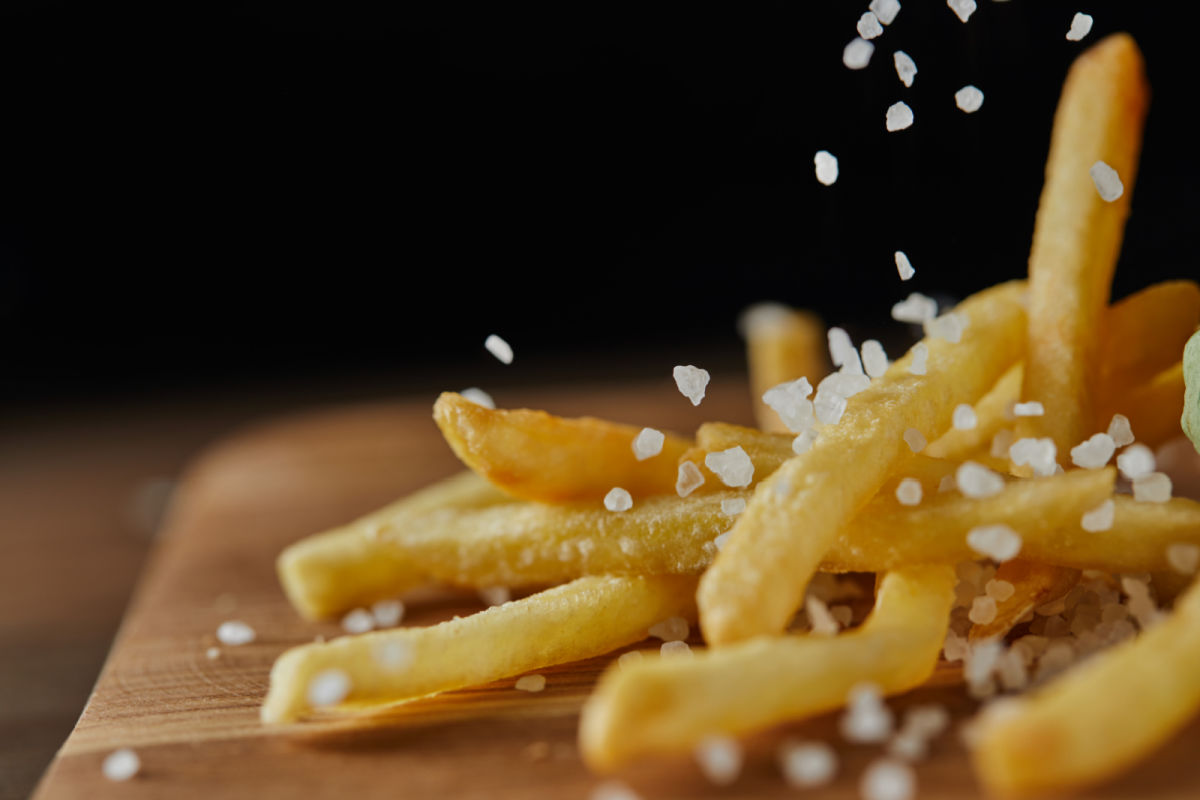 Wooden board with restaurant quality french fries and a sprinkling of coarse sea salt.