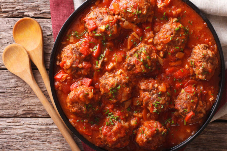 Overhead view of a black casserole dish with baked Italian meatballs simmered in marinara sauce and garnished with chopped fresh parsley.