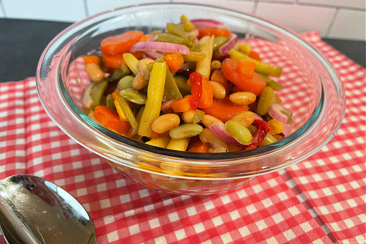 Clear bowl of Grandma's Pickled Vegetable Salad on a red and white gingham napkin.