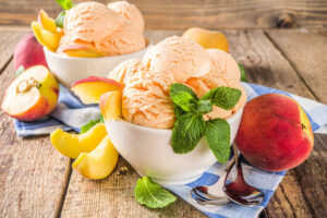 Several scoops of Sweet Georgia Peach Ice Cream in small bowls, on wooden background with fresh peaches and mint leaves