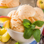 Several scoops of Sweet Georgia Peach Ice Cream in small bowls, on wooden background with fresh peaches and mint leaves