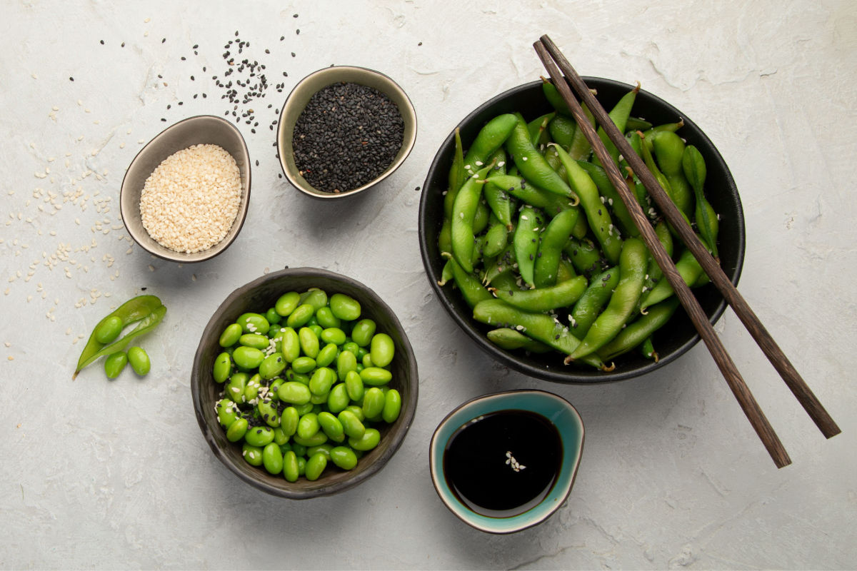 Bowl of Asian Steamed Edamame in the pods with sesame seeds and soy sauce. There is also a bowl of shelled edamame.