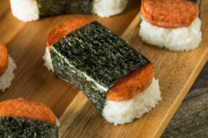 Wooden board with several Spam Sushi (Musubi) - handheld treat of sushi rice and teriyaki glazed Spam wrapped in nori.
